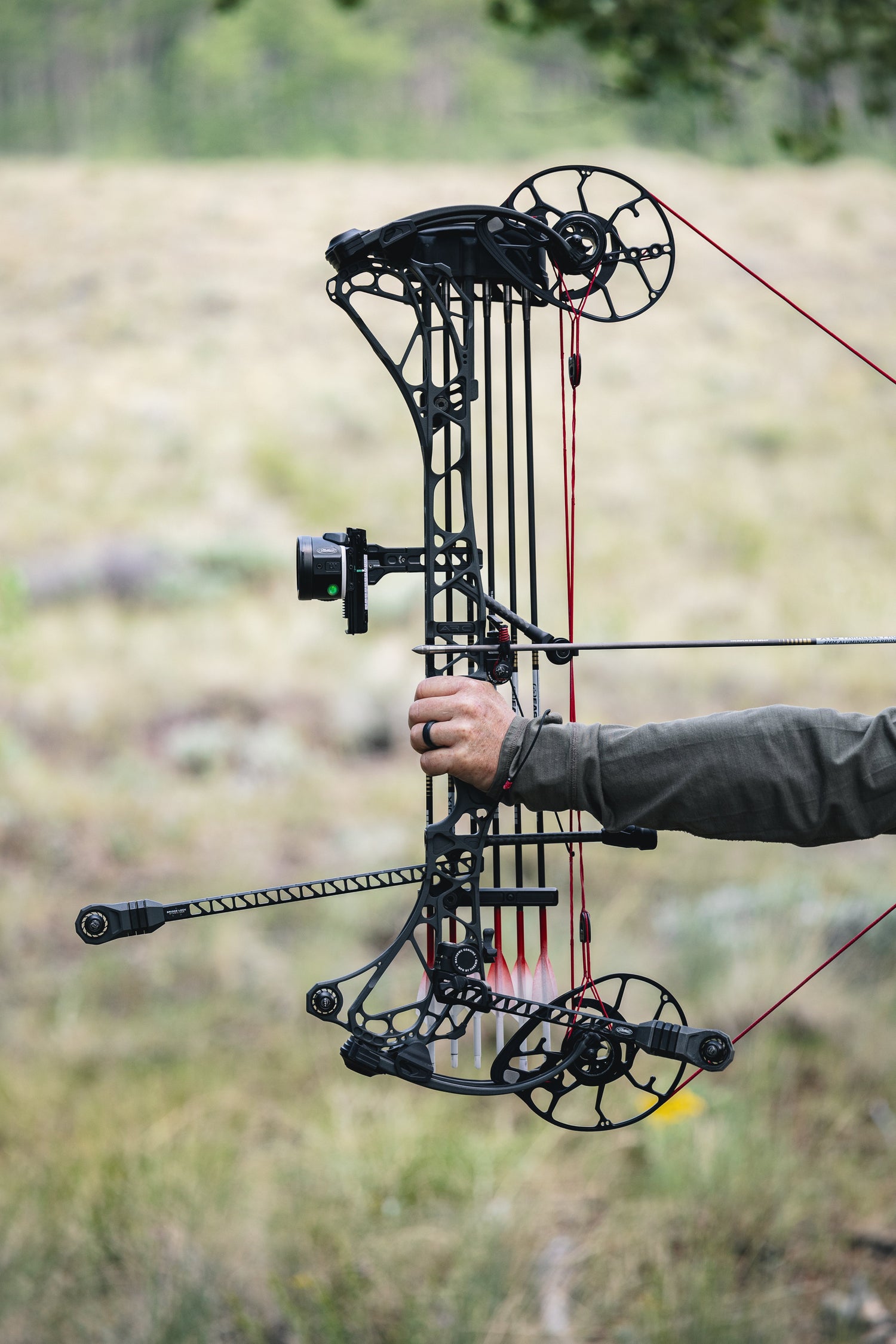 Archer drawing back a Mathews ARC compound bow with a blurred field background